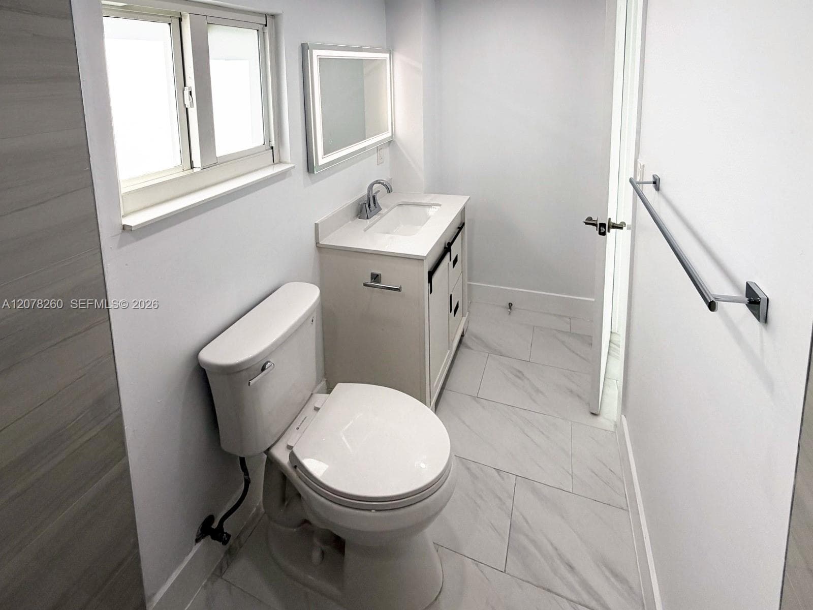 Bathroom featuring large-format tile flooring, a white vanity with a composite countertop and integrated sink, an LED-backlit mirror, and chrome hardware