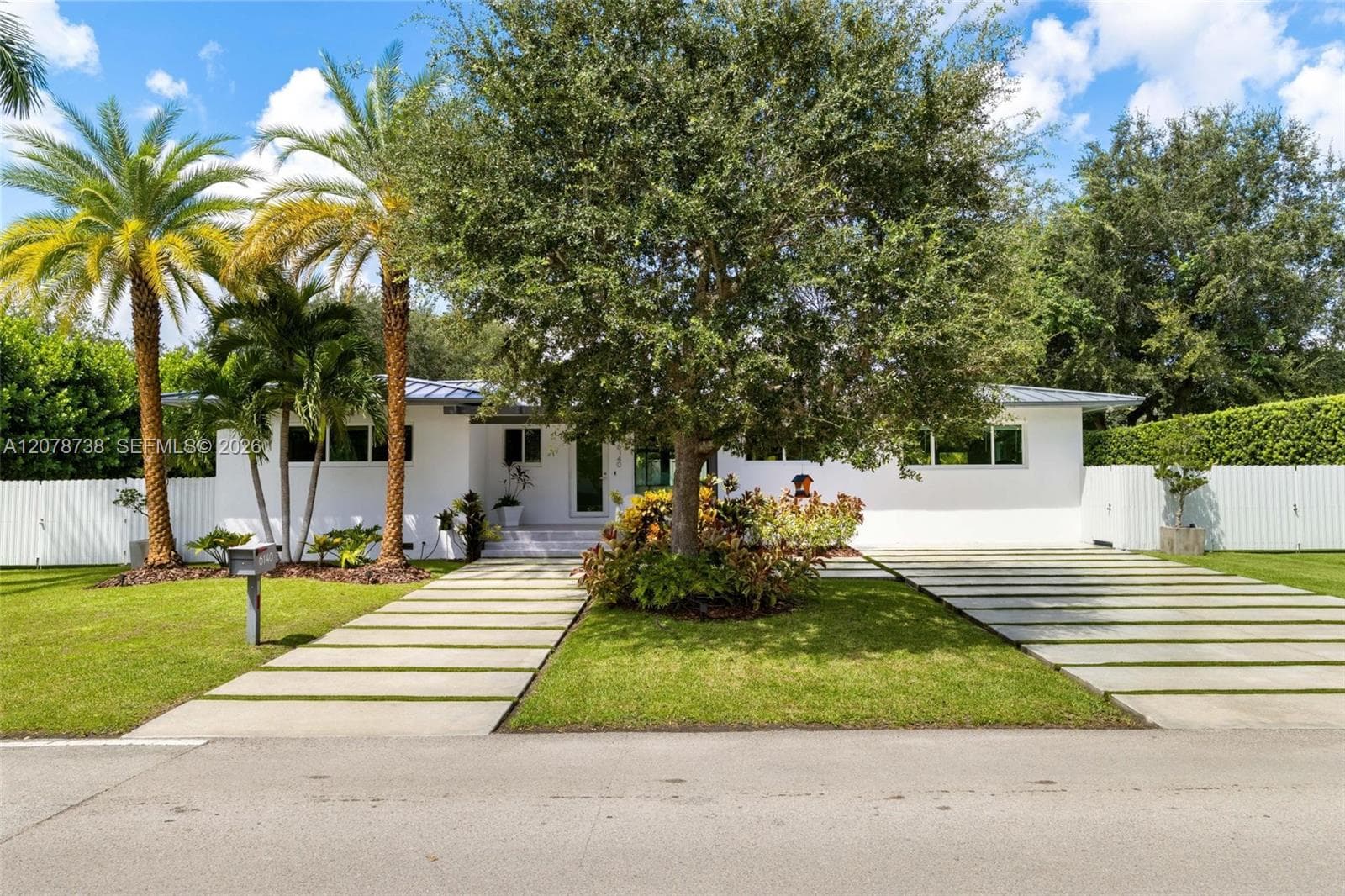 A modern metal roof, crisp white exterior, oversized stepping-stone driveway and lush greenery create a contemporary first impression without losing the warmth of a true neighborhood home.