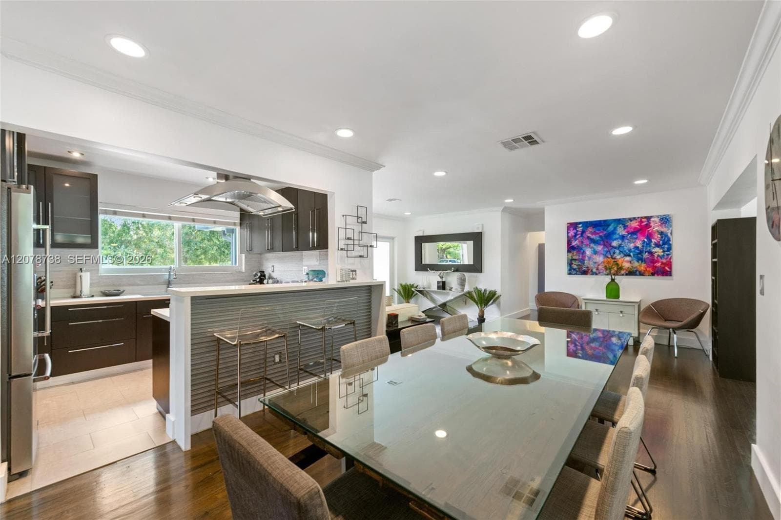 Dark cabinetry contrasts against bright countertops and stainless-steel appliances, while the open breakfast bar connects the kitchen directly to the dining and living areas.