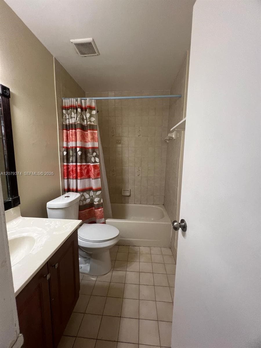 Bathroom featuring a vanity with wood-finish cabinetry, a white countertop with an integrated sink, a tiled bathtub surround, and light-toned floor tiling