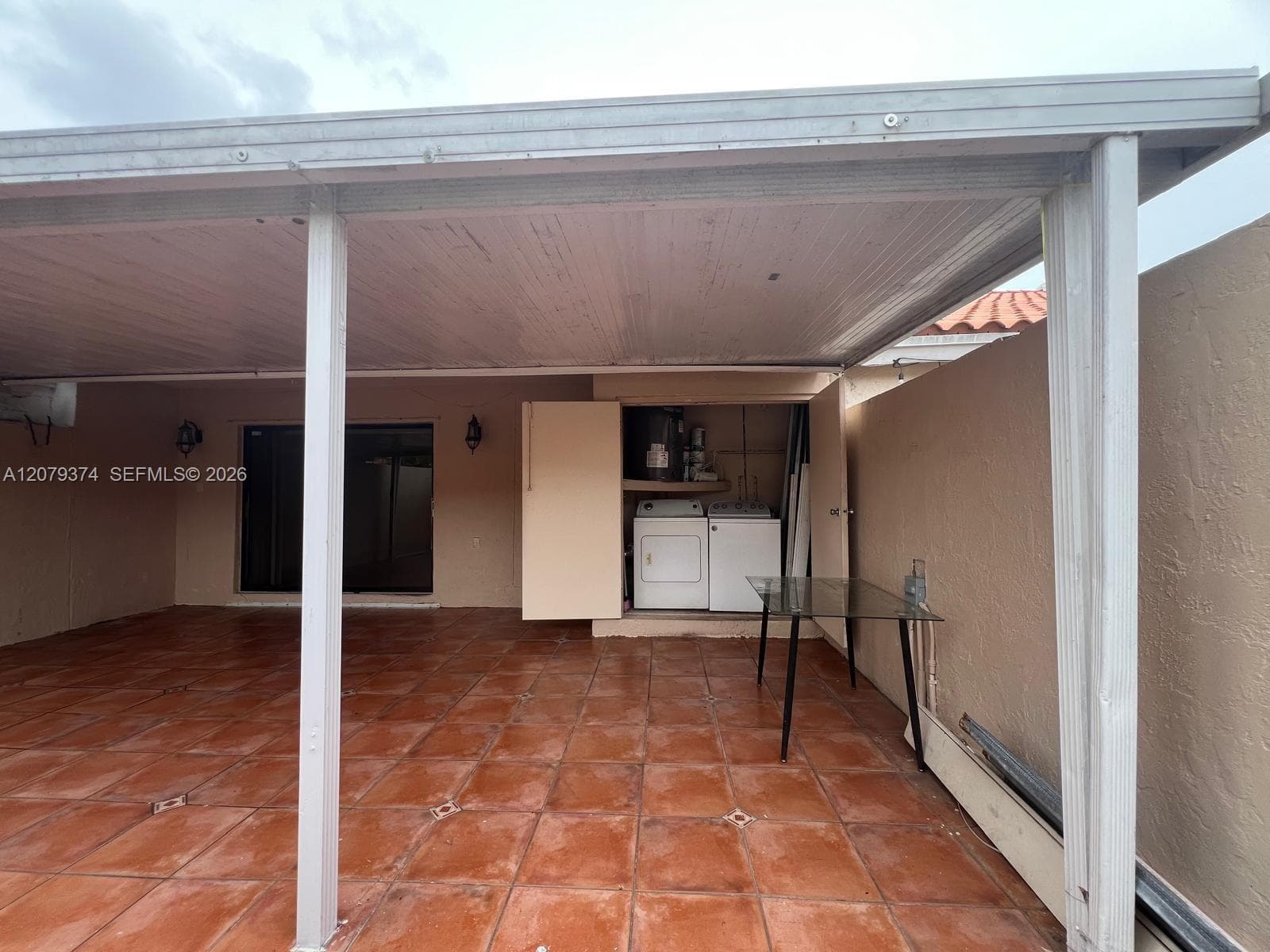 Covered outdoor patio featuring tile flooring, a flat-roof structure, and an integrated laundry enclosure