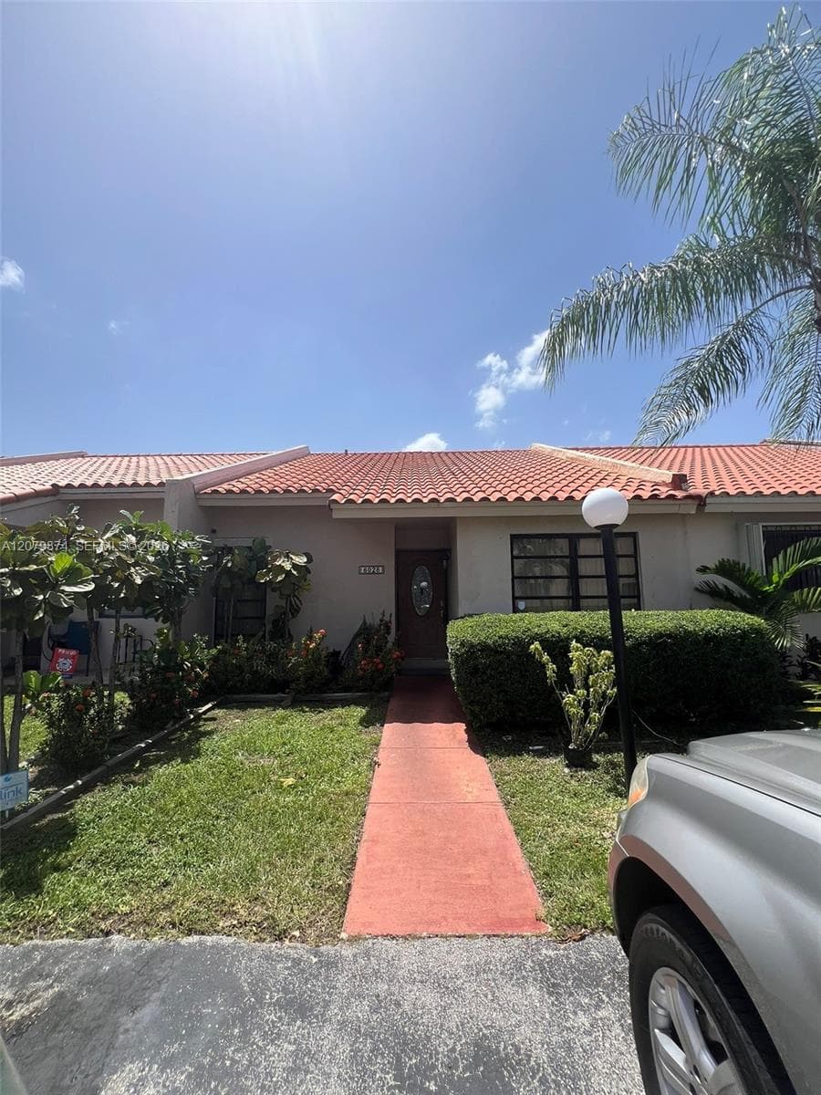 Single-story exterior featuring a terracotta-style tiled roof, a painted stucco facade, a straight-path paved walkway, and an oval-insert front entry door