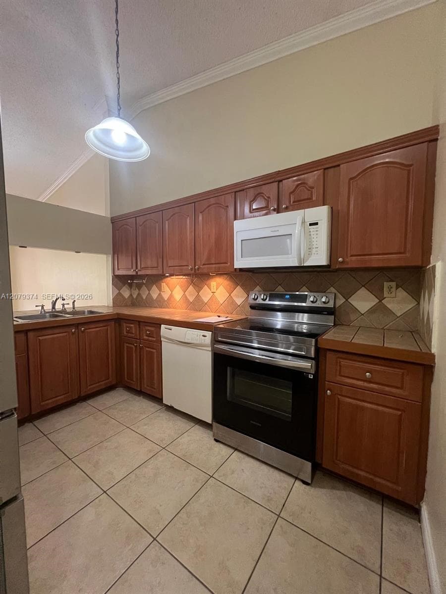 Kitchen featuring wood cabinetry, tile countertops, diamond-pattern tile backsplash, stainless steel range, and ceramic tile flooring