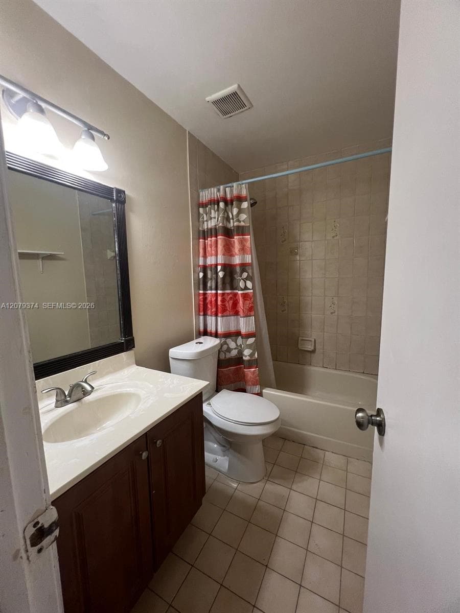 Bathroom featuring a vanity with an integrated sink, dark-toned cabinetry, a framed vanity mirror, and tile flooring