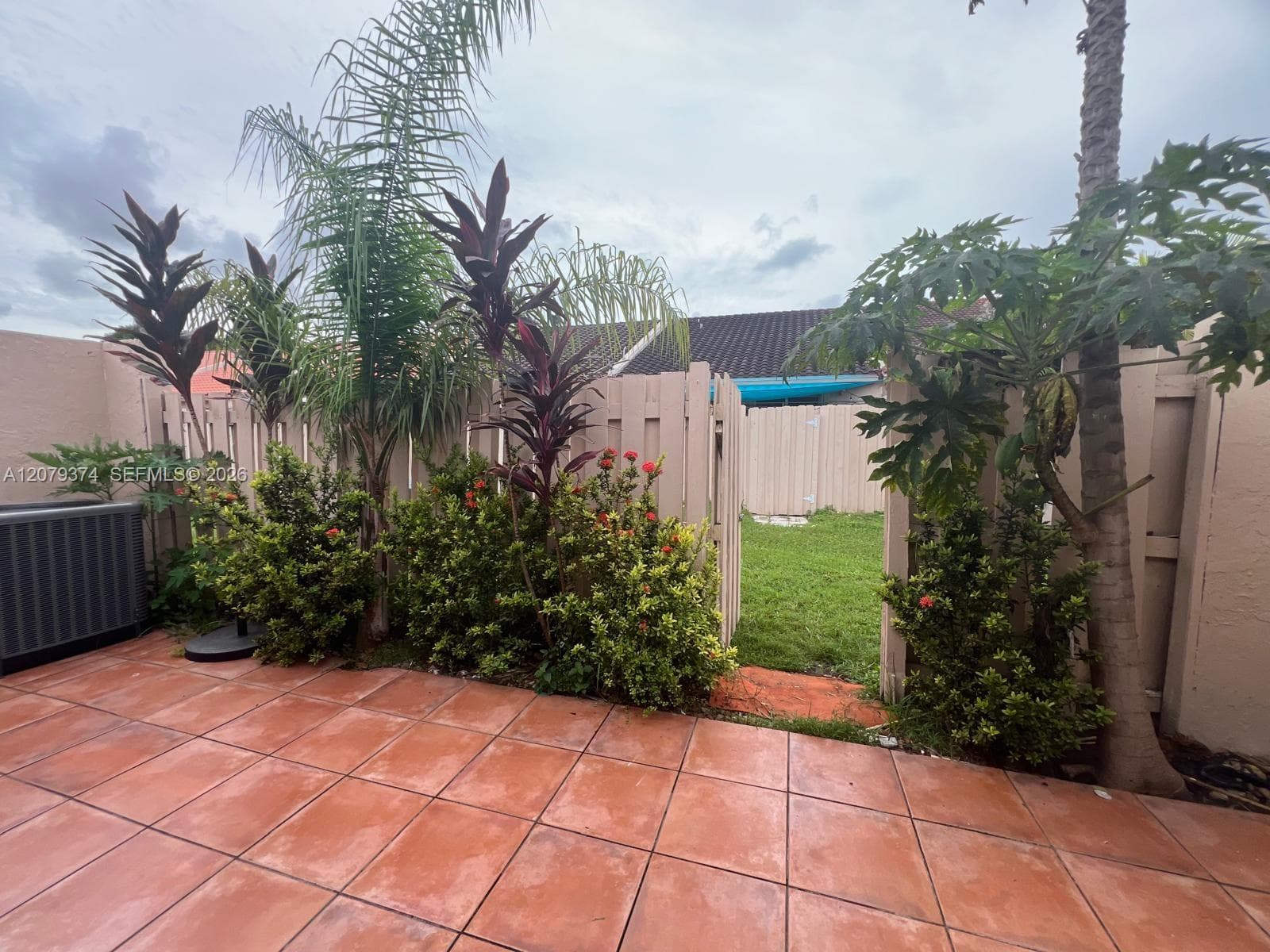 Outdoor patio featuring terracotta-style tiling, perimeter privacy fencing, and established tropical landscaping