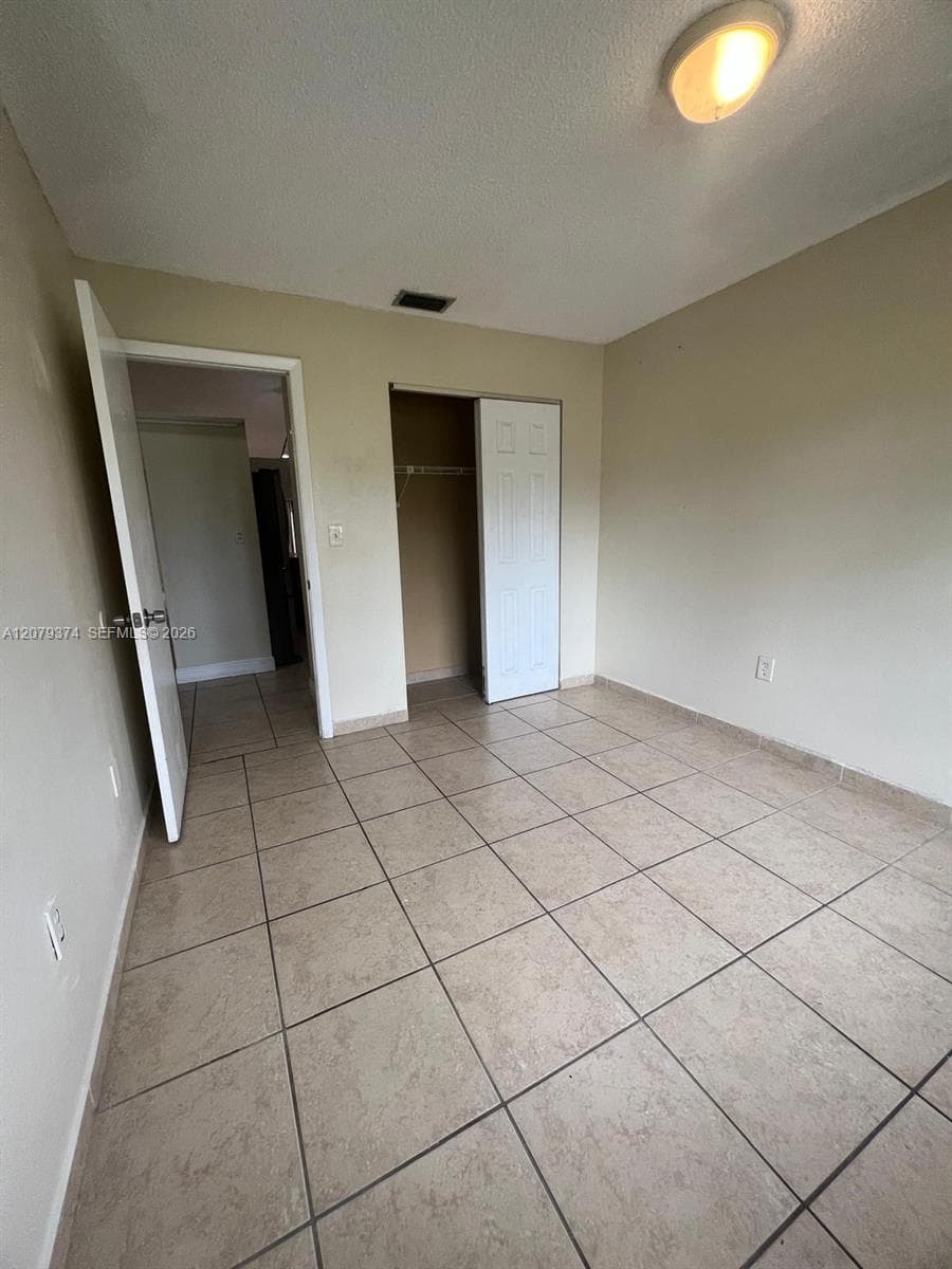 Neutral-toned interior space featuring square ceramic tile flooring, a recessed closet with a six-panel door, and a dome-style flush mount ceiling light fixture