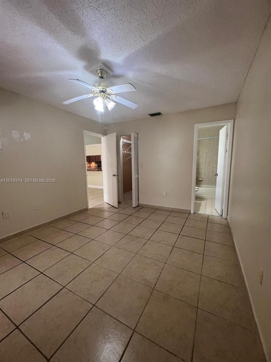 Neutral-toned interior space featuring ceramic tile flooring, a multi-blade ceiling fan with integrated lighting, and dual entry points to dedicated storage and utility areas
