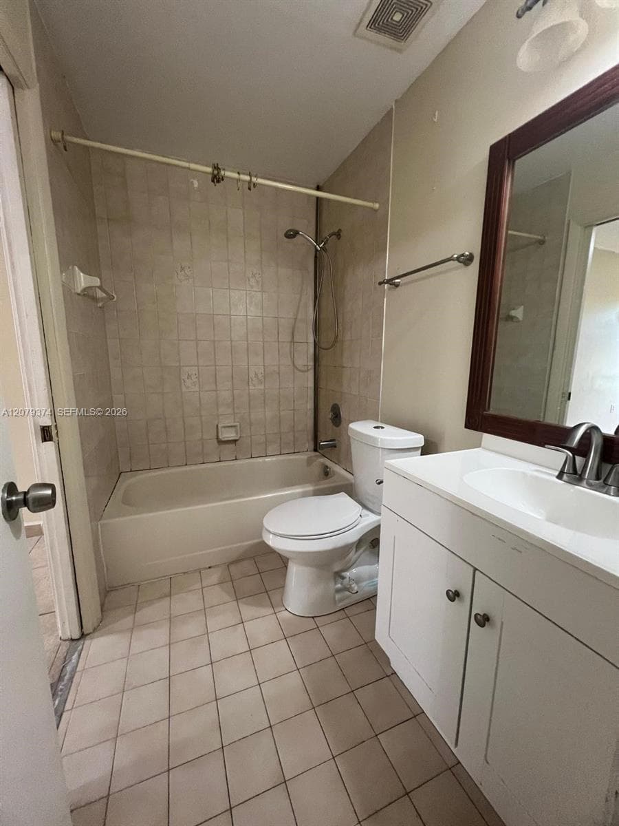 Bathroom featuring a vanity with an integrated white sink, wall-mounted mirror with a dark-finish frame, ceramic tile flooring, and a shower-tub combination with tiled surround
