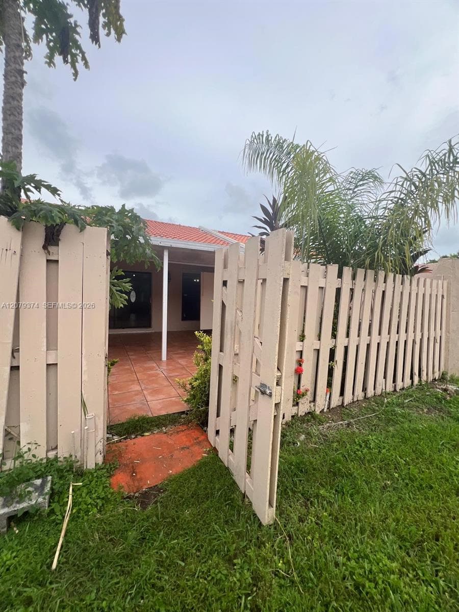 Private courtyard featuring a tiled patio, secure wood fencing, and mature tropical landscaping