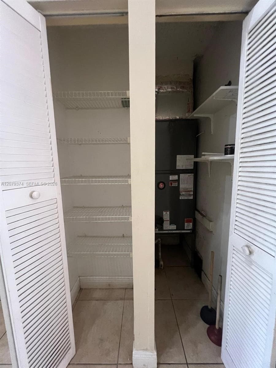 Storage closet featuring white louvered doors, white wire shelving, and tile flooring