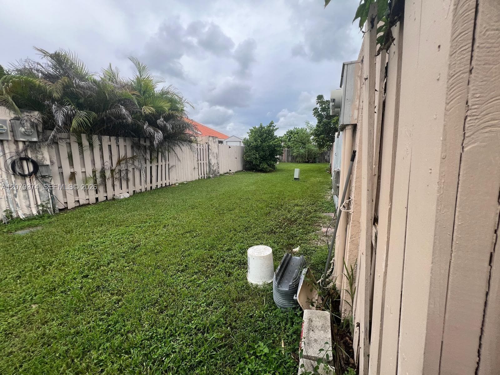 Fenced outdoor side yard featuring a grass lawn, mature palm foliage, and vertical privacy fencing