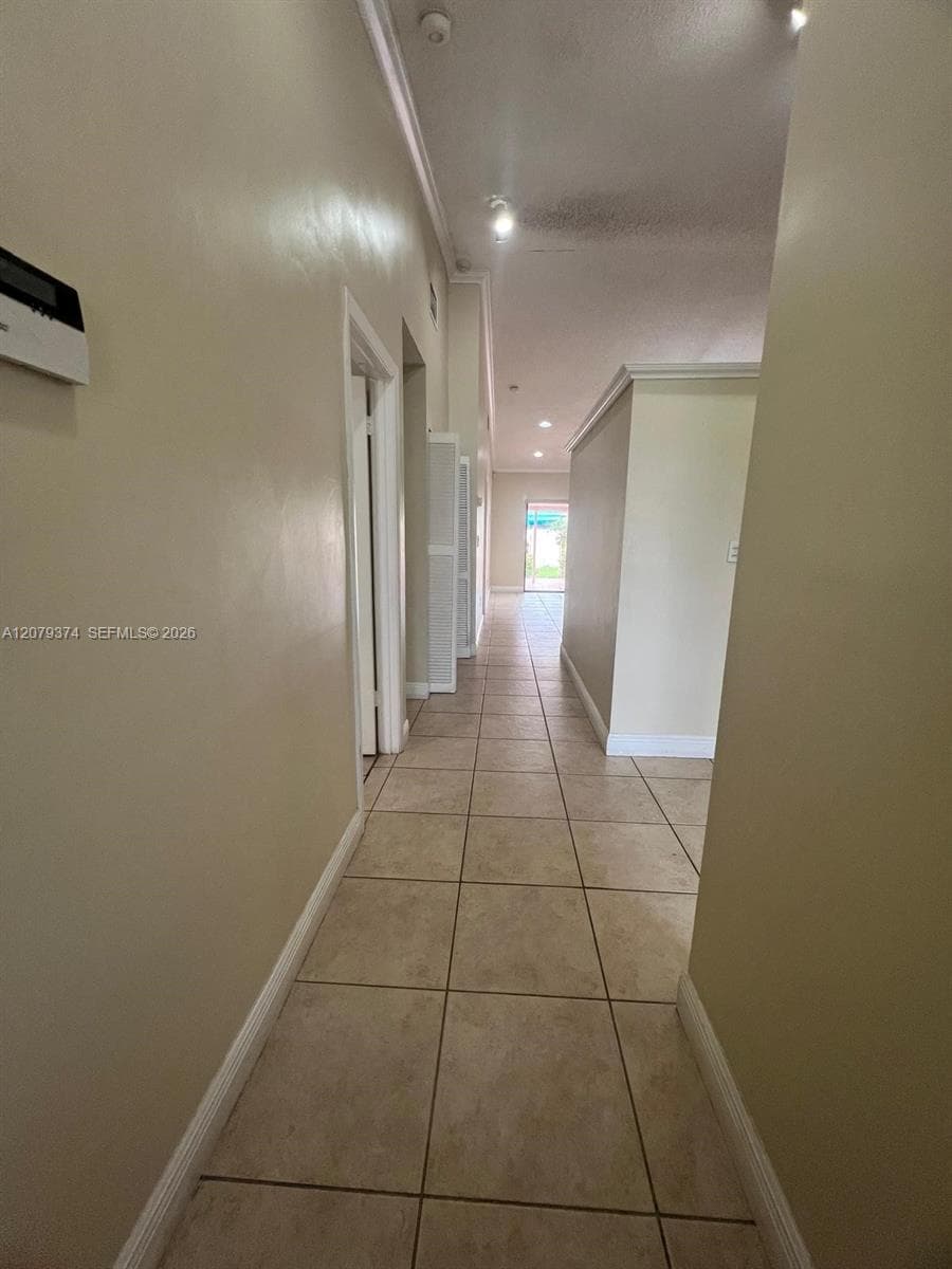 Neutral-toned hallway featuring large-format ceramic tile flooring, recessed lighting, and crown molding