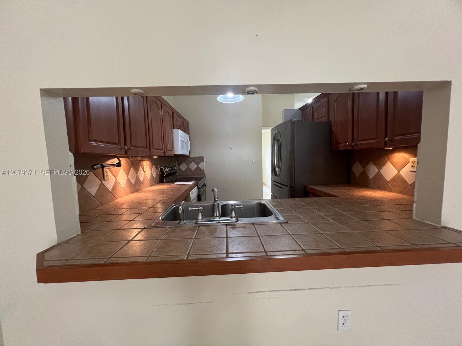 Kitchen featuring wood cabinetry, tiled countertops, a dual-basin stainless steel sink, tile backsplash, and recessed lighting
