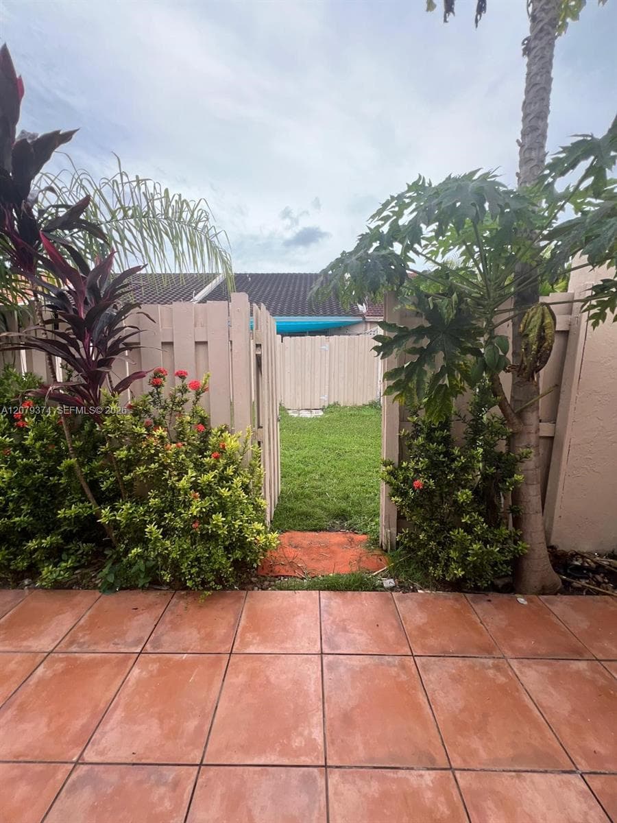 Private backyard featuring a paved tile patio, grass lawn, privacy fencing, and mature landscaping
