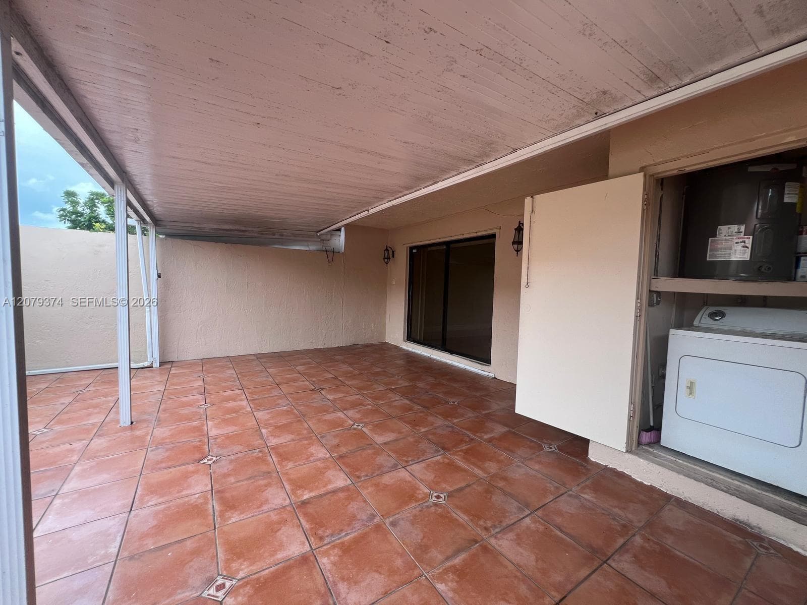 Covered patio featuring terra cotta tile flooring, a solid ceiling structure, and an integrated exterior utility closet with built-in laundry hookups