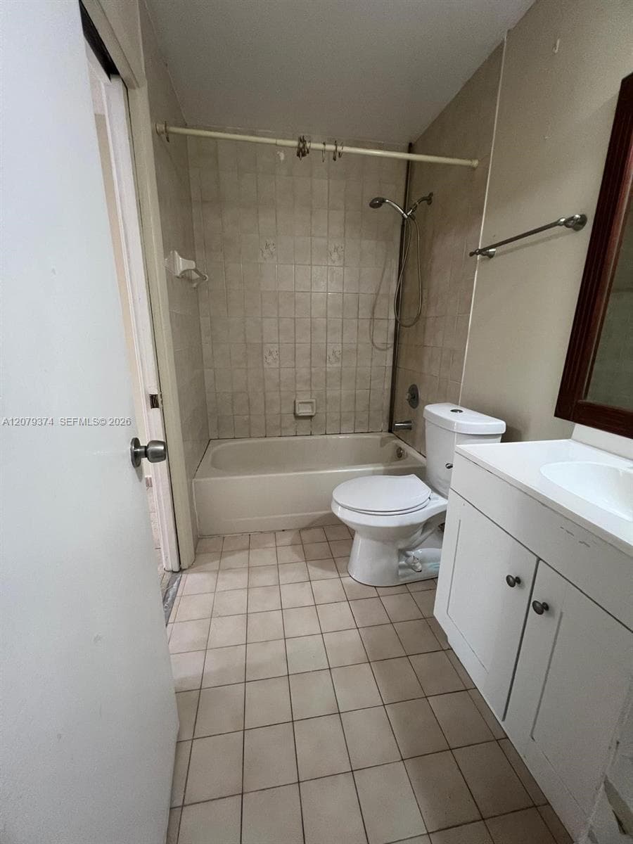 Bathroom featuring tile flooring, tub-shower combination with tiled surround, white vanity cabinet with integrated sink, and dual-handle plumbing fixtures
