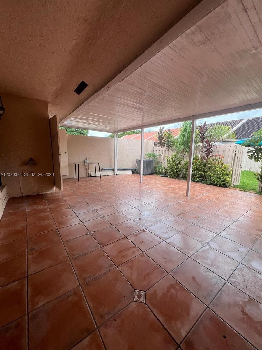 Covered patio featuring terra cotta tile flooring, a solid roof structure, and a fenced perimeter