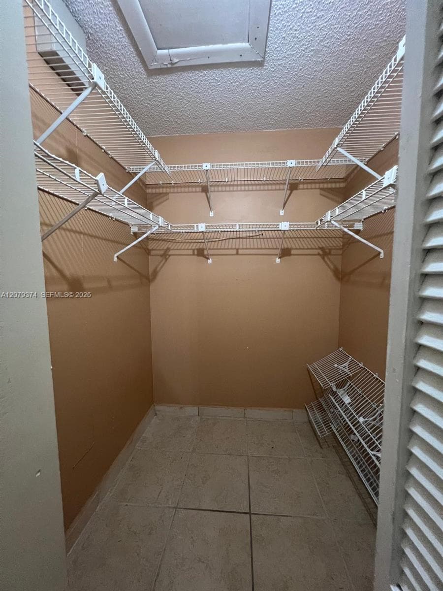 Storage closet featuring multi-level white wire shelving, floor-to-ceiling neutral wall surfaces, tile flooring, and louvered folding doors