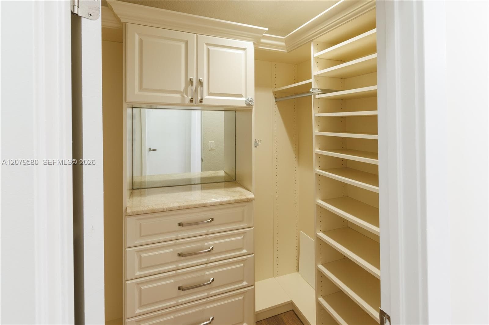Walk-in closet featuring custom built-in cabinetry, stone-top vanity with integrated mirror, adjustable shelving, and hanging rods