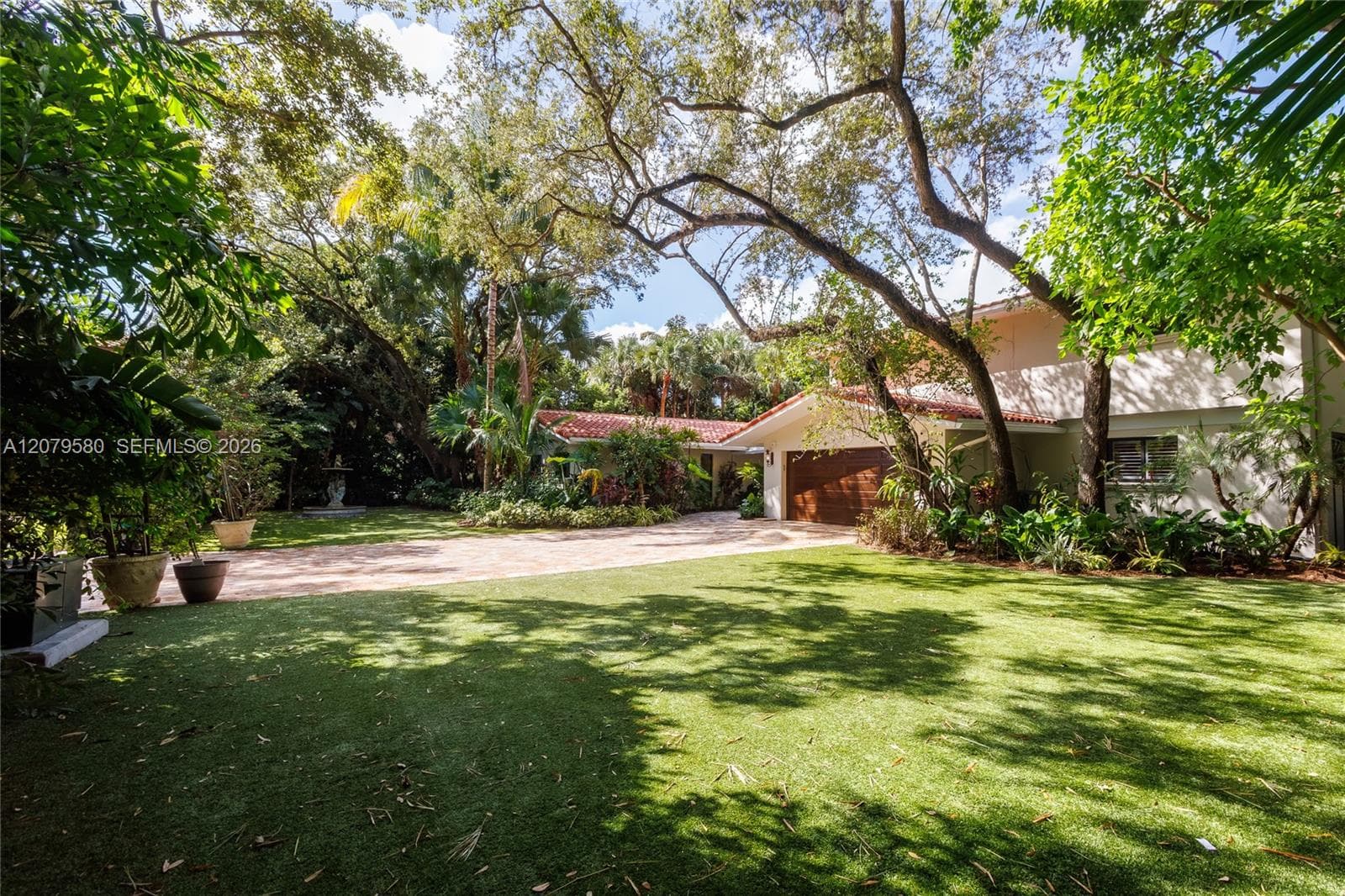 Expansive exterior featuring a tiled roof, paved circular driveway, mature oak trees, and integrated two-car garage