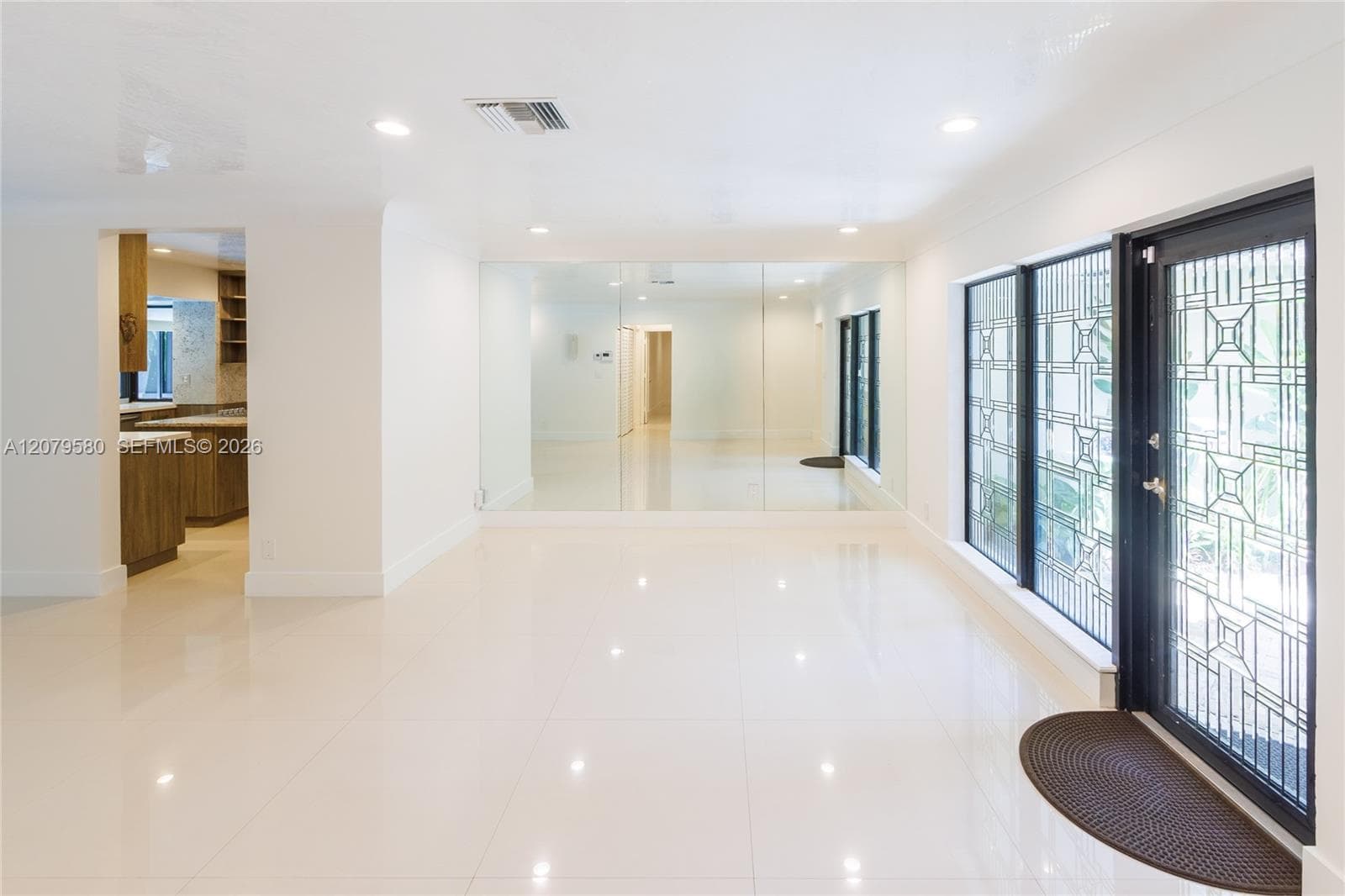 Interior space featuring polished tile flooring, recessed lighting, floor-to-ceiling wall mirrors, and an exterior door with geometric glass inlay