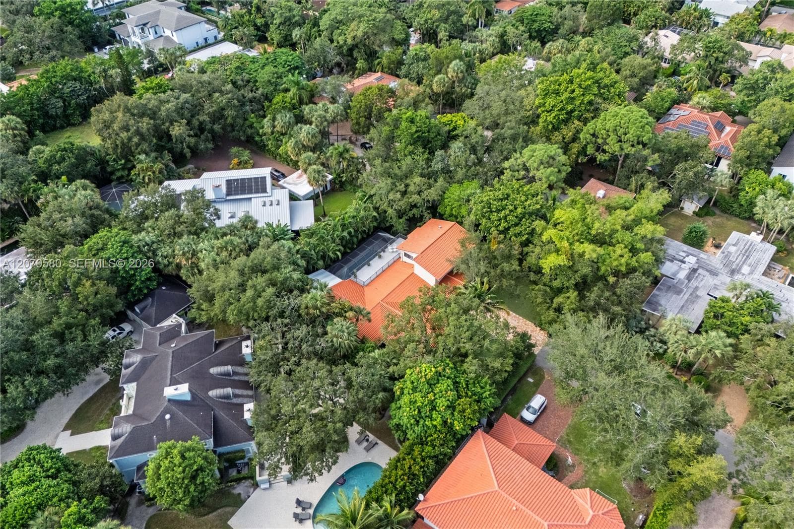 Aerial perspective featuring a multi-structure property with terracotta tile roofing, mature canopy trees, and established landscaping