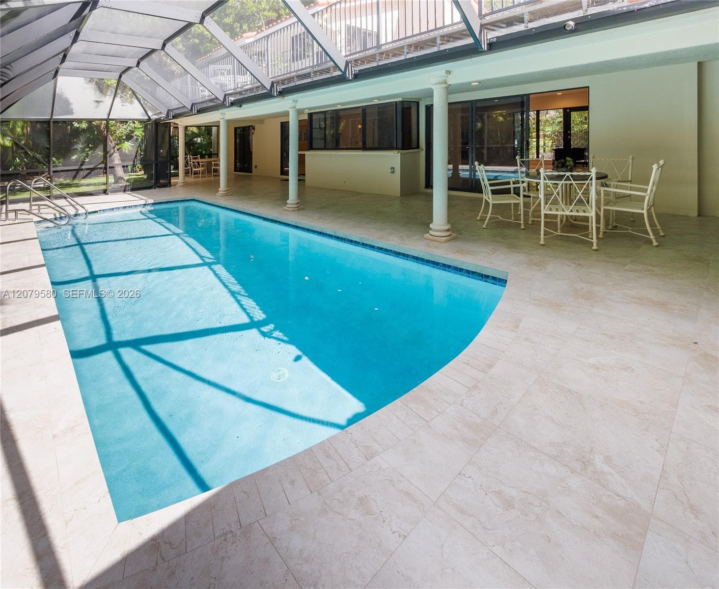 Screened-in pool area featuring light-toned tile decking, built-in columns, and sliding glass entry doors