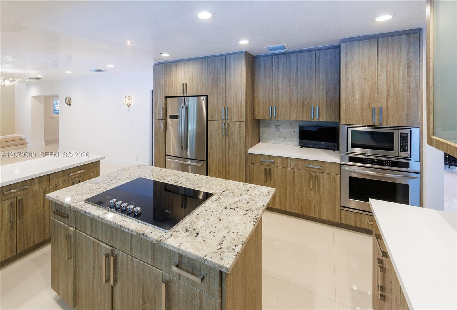 Kitchen featuring wood-finish cabinetry, stone countertops, central island with integrated cooktop, stainless steel appliances, and built-in wall oven