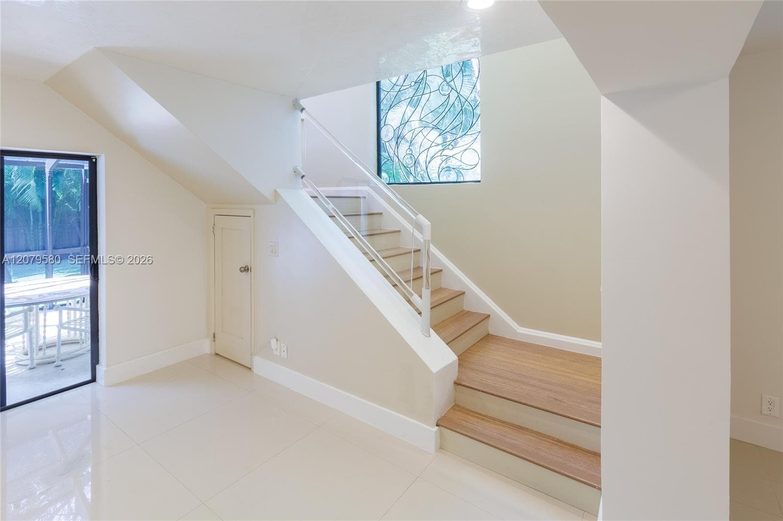 Staircase featuring wood-finish treads, a white metal railing, and a decorative wrought-iron window accent
