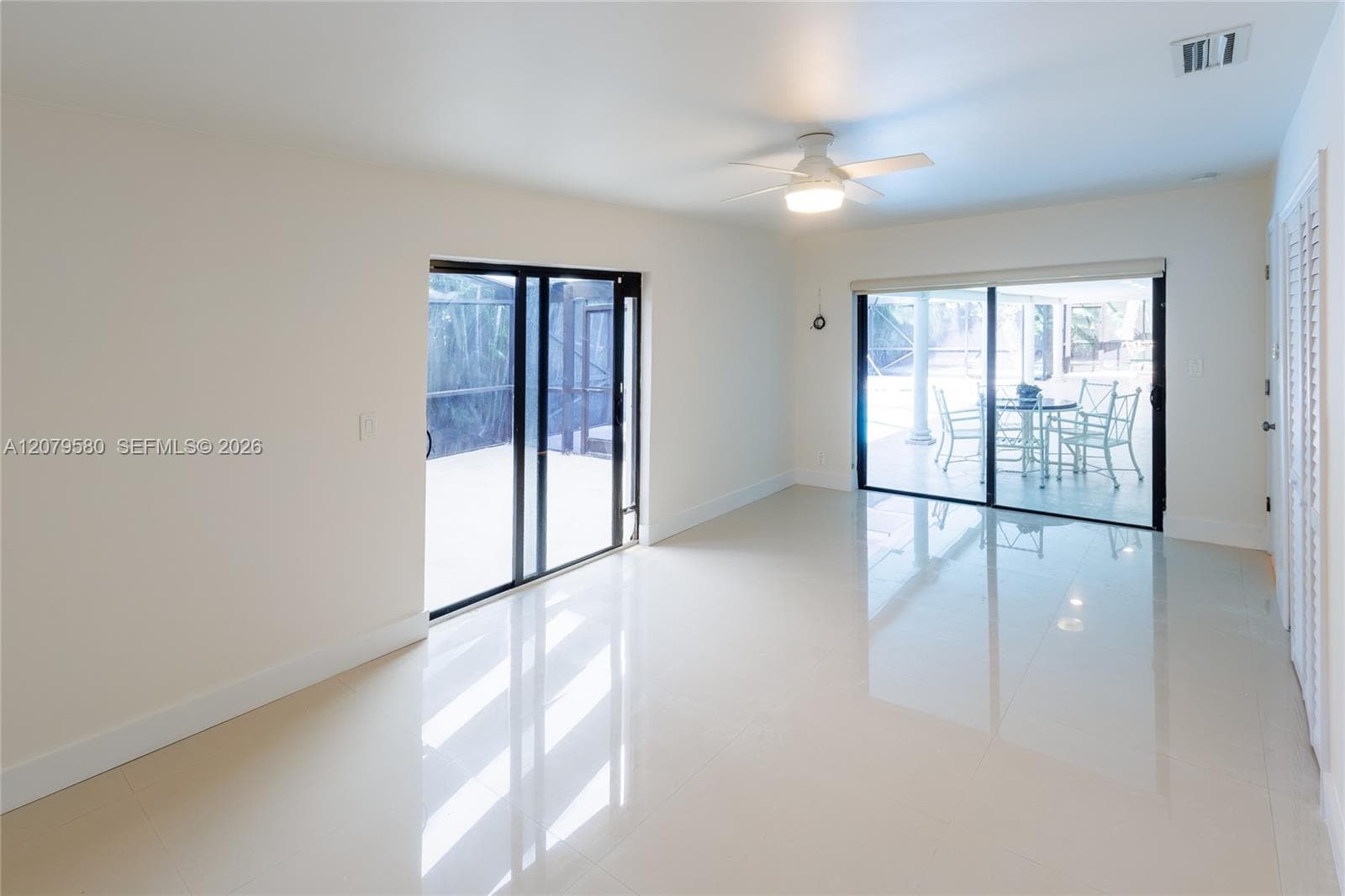 Interior space featuring polished tile flooring, two sets of black-framed sliding glass doors, a ceiling fan with integrated lighting, and louvered closet doors