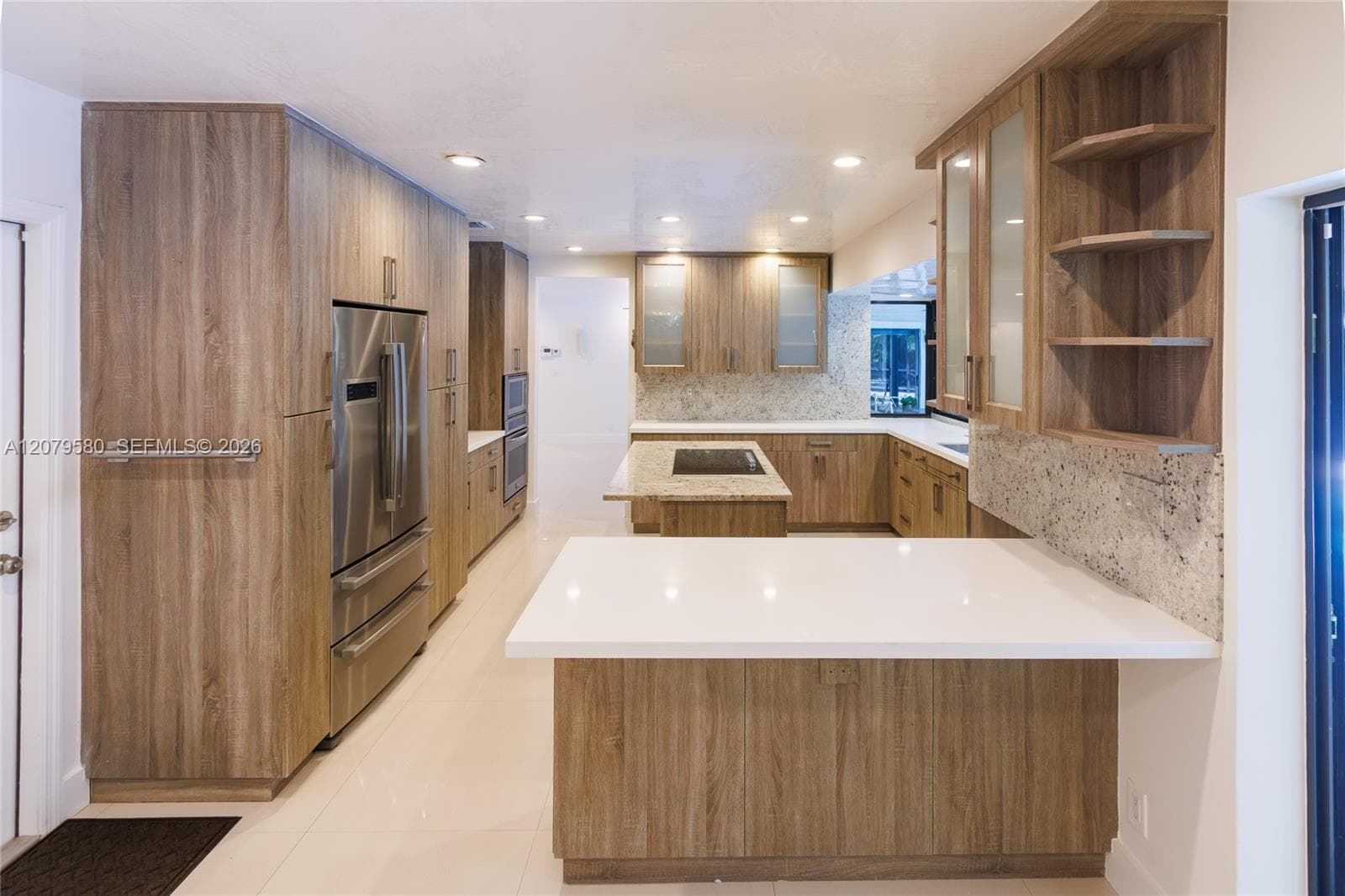 Kitchen featuring wood-finish cabinetry, stone slab countertops, a central island with a built-in cooktop, stainless steel refrigerator, and recessed lighting