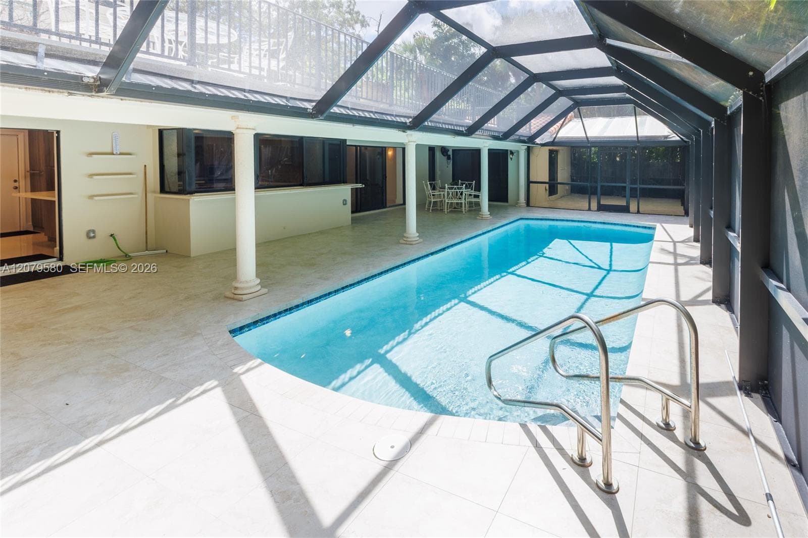 Enclosed swimming pool area featuring a screen cage, tile deck, built-in bar counter, and column supports