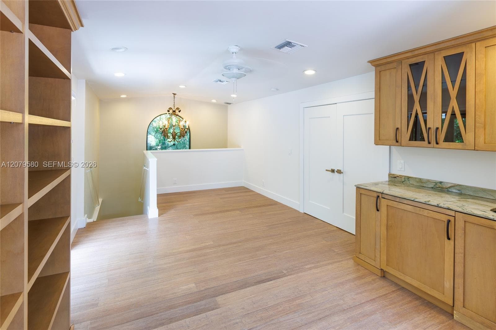 Built-in shelving, wood-finish cabinetry with glass-front detailing, stone-surface countertop, recessed lighting, and an arched window fixture