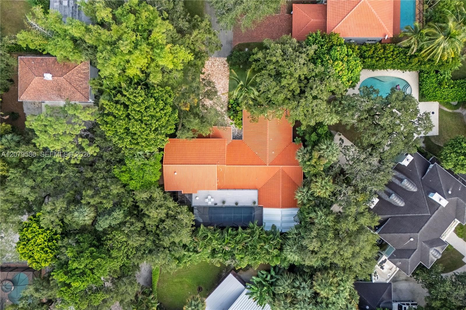 Aerial view of property featuring a multi-pitched clay tile roof, mature canopy trees, and an integrated solar panel array