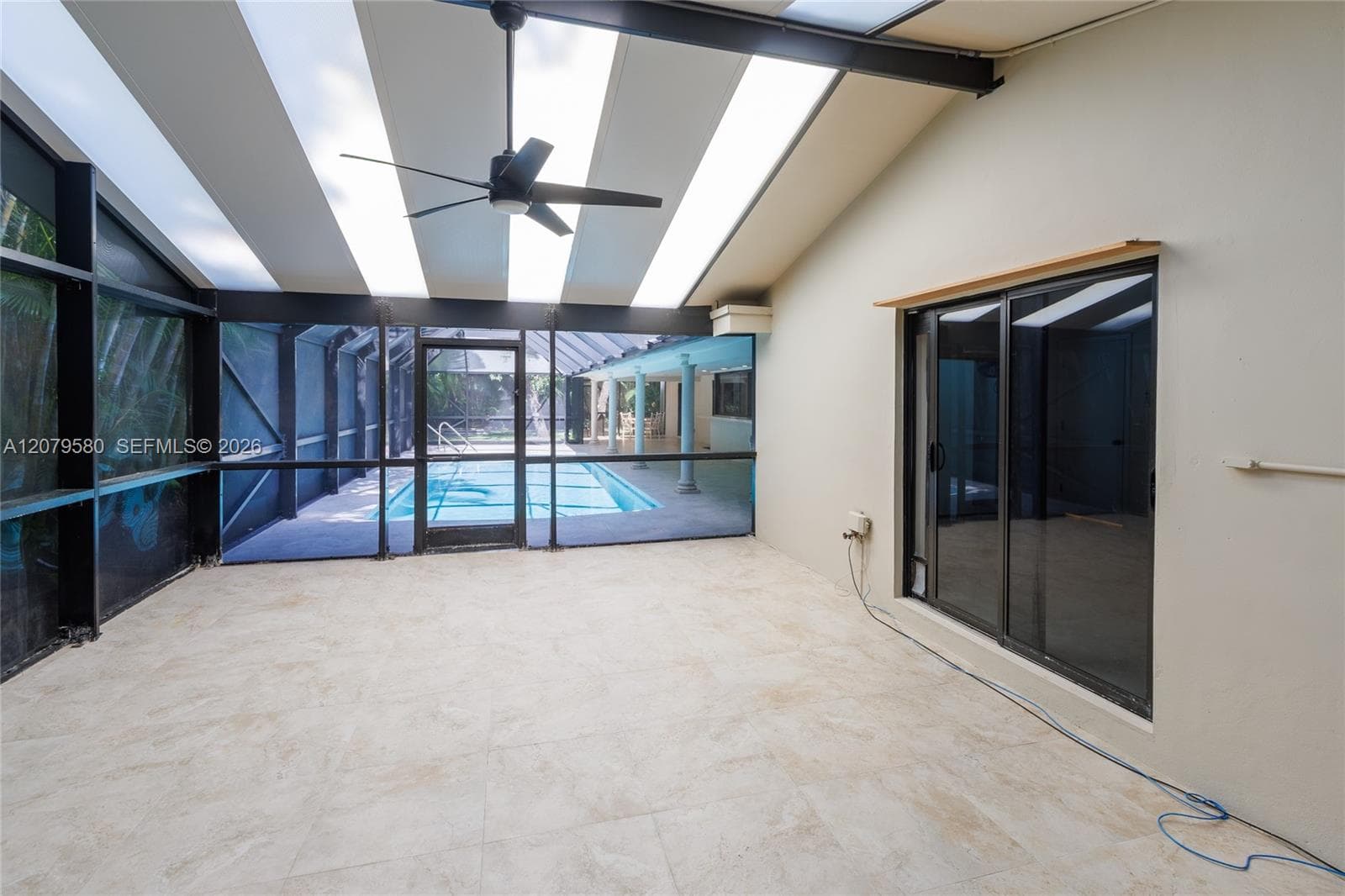 Enclosed patio featuring light-toned floor tile, a sloped ceiling with integrated skylights, a ceiling fan, and sliding glass doors, overlooking a screened-in swimming pool