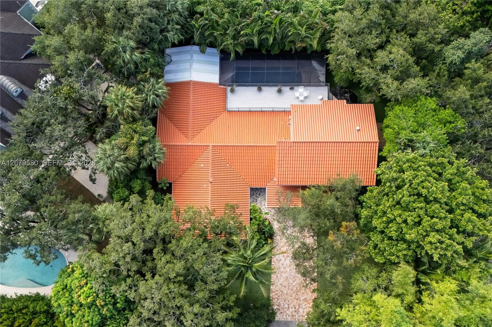 Aerial perspective featuring a multi-gabled clay tile roof, screened lanai with pool, and stone-paved driveway surrounded by mature landscaping