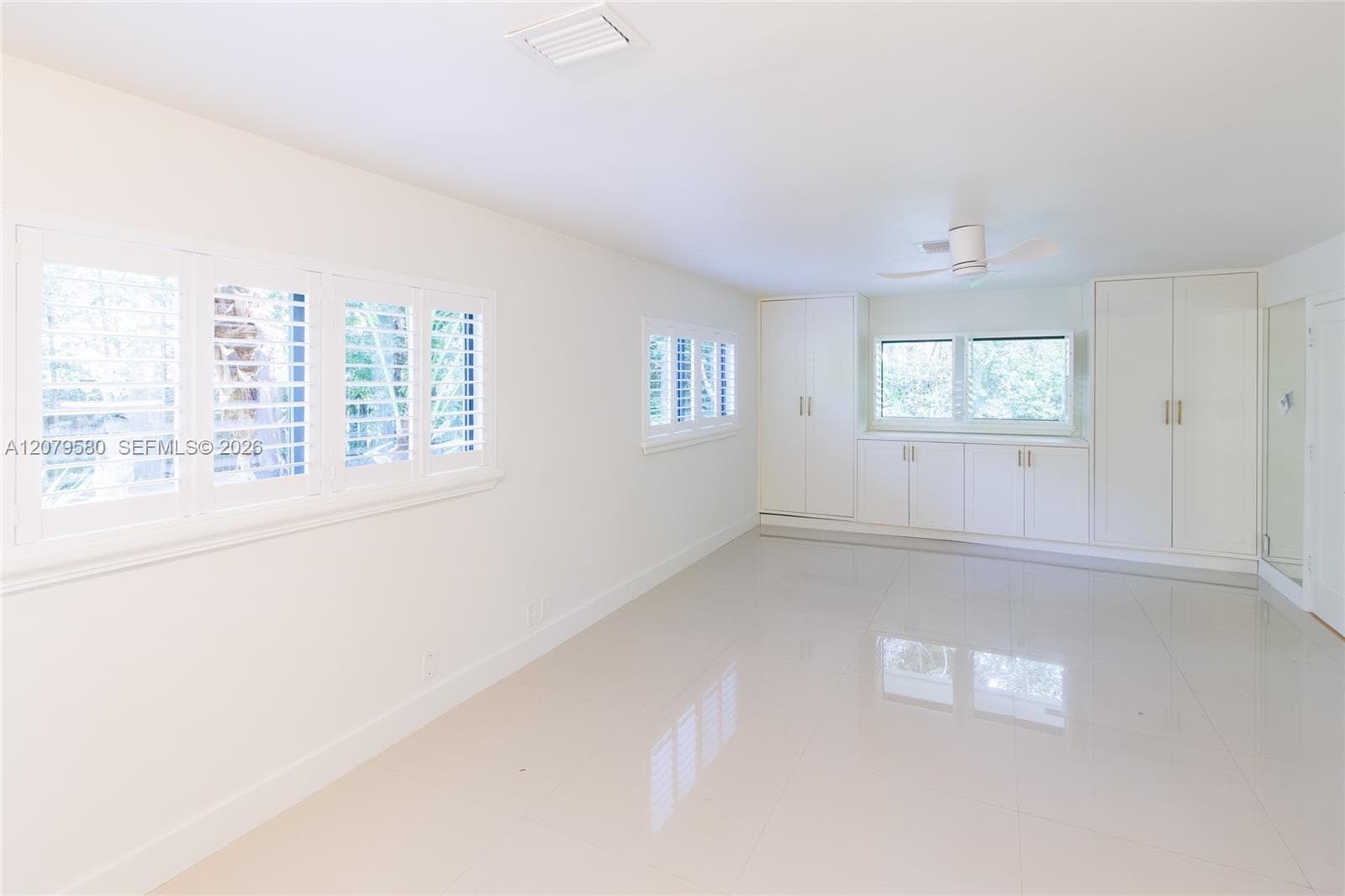 Neutral-toned tile flooring, custom built-in white cabinetry, louvered plantation shutters, and a ceiling-mounted fan