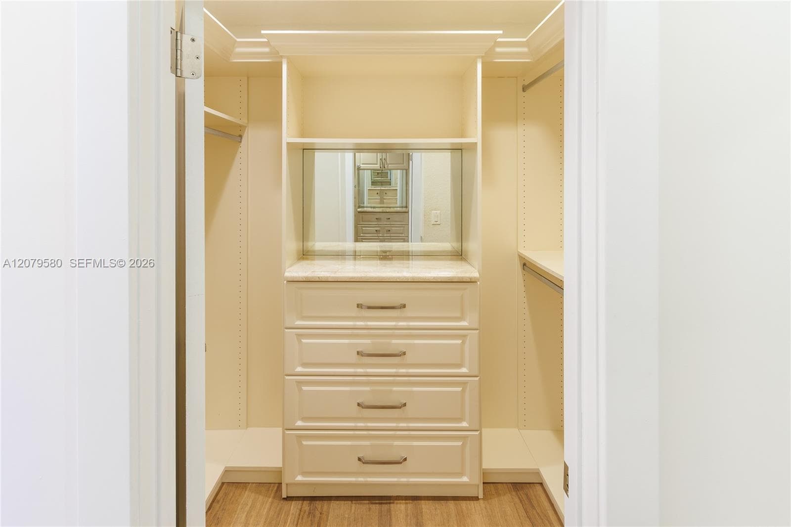Walk-in closet featuring custom cabinetry with four soft-close drawers, a stone-surface countertop, an inset wall mirror, crown molding, and hanging rods