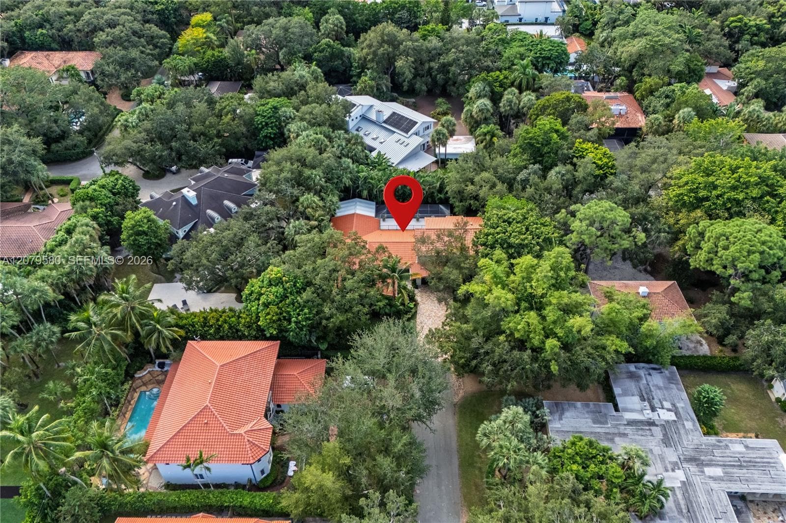 Aerial perspective of a property featuring a clay tile roof and a paved driveway, surrounded by mature trees and dense vegetation