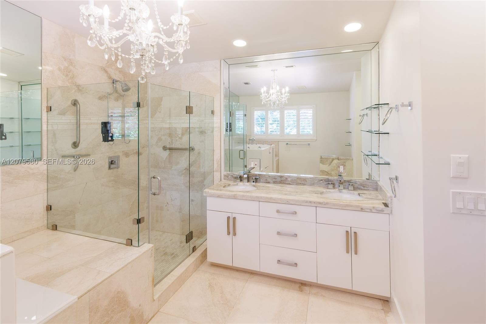 Bathroom featuring a double-sink vanity with stone countertop, walk-in glass-enclosed shower, large wall-to-wall mirror, crystal chandelier, and integrated glass shelving