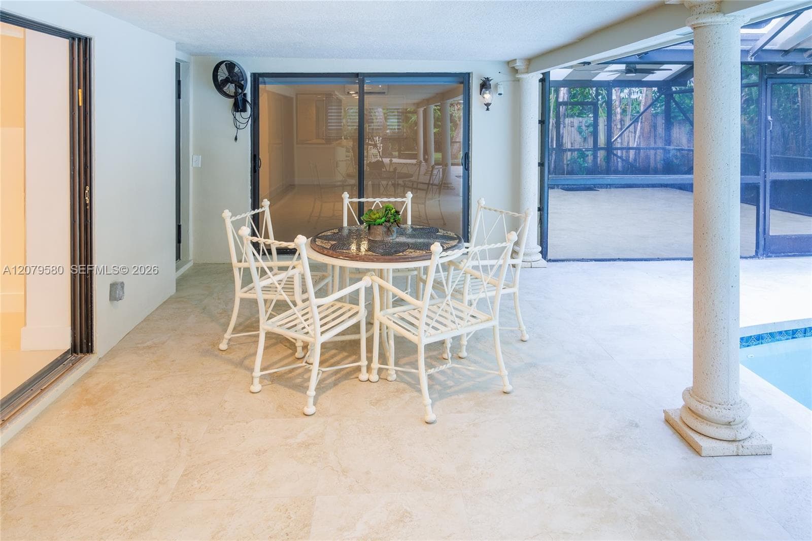 Covered patio featuring large-format stone-style flooring, structural decorative columns, and full-height sliding glass doors opening to a screened enclosure with a pool