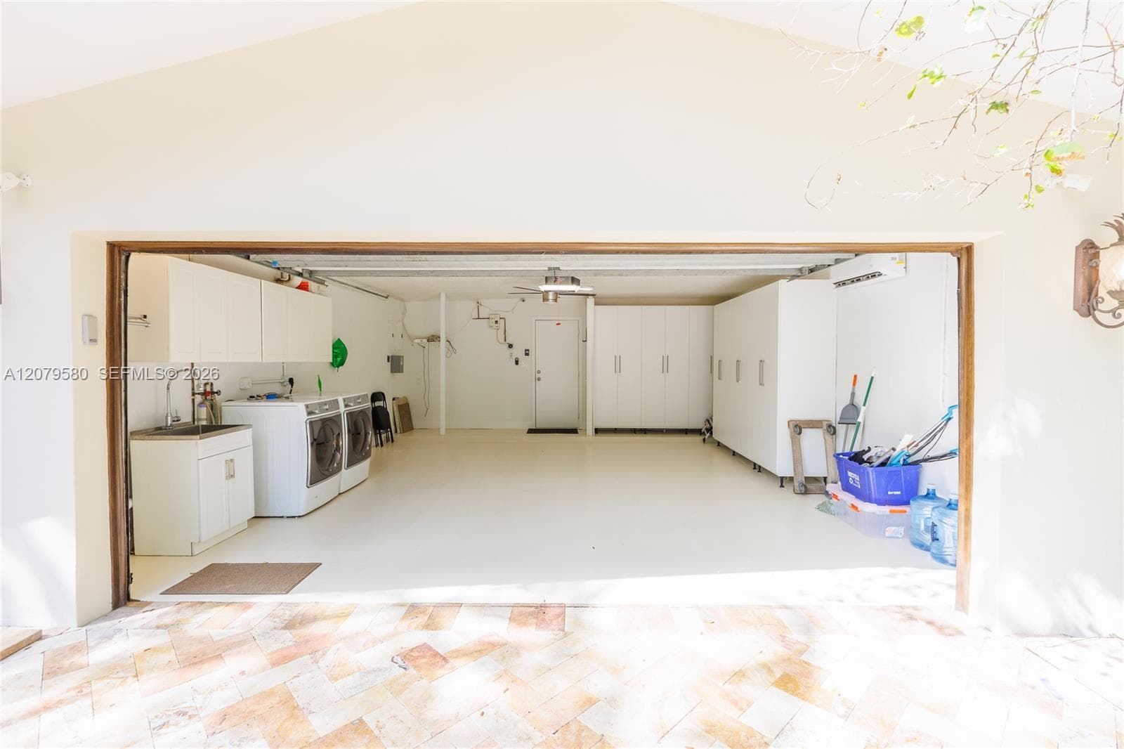 Two-car garage featuring epoxy flooring, built-in cabinetry, a utility sink, and a wall-mounted climate control unit