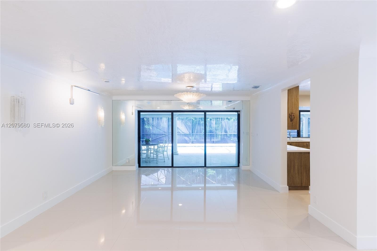 Interior space featuring polished stone flooring, floor-to-ceiling mirrored panels, a central multi-arm ceiling fixture, and sliding glass doors