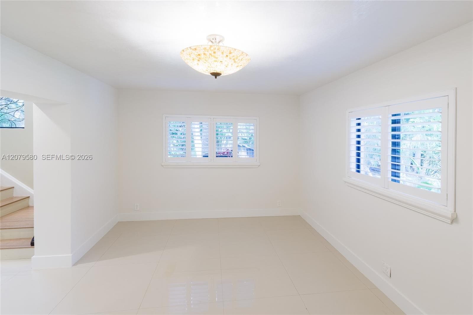 Interior space featuring neutral tile flooring, two windows with white plantation shutters, and a decorative semi-flush mount ceiling fixture