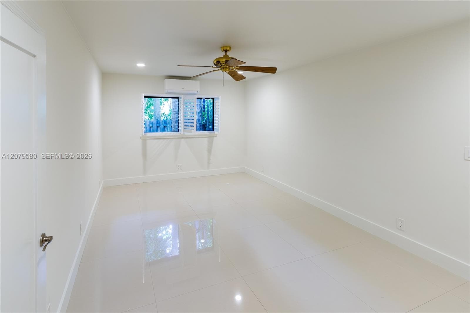 Neutral-toned tile flooring, recessed ceiling lighting, wall-mounted ductless air conditioning unit, ceiling fan with wood-finish blades, and plantation shutters