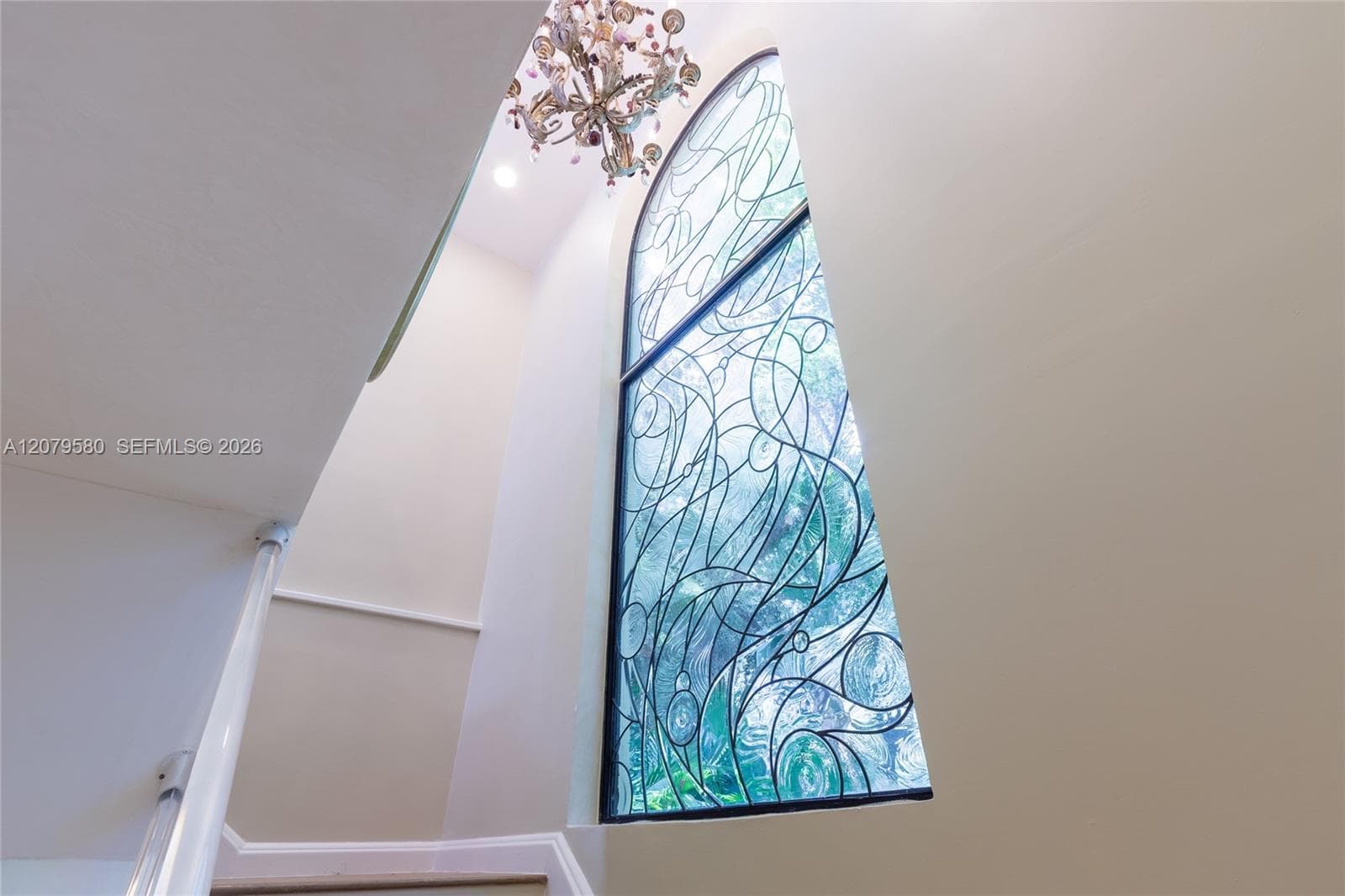 Arched, floor-to-ceiling stained glass window featuring intricate leaded detailing, paired with a multi-tiered crystal chandelier and recessed ceiling lighting