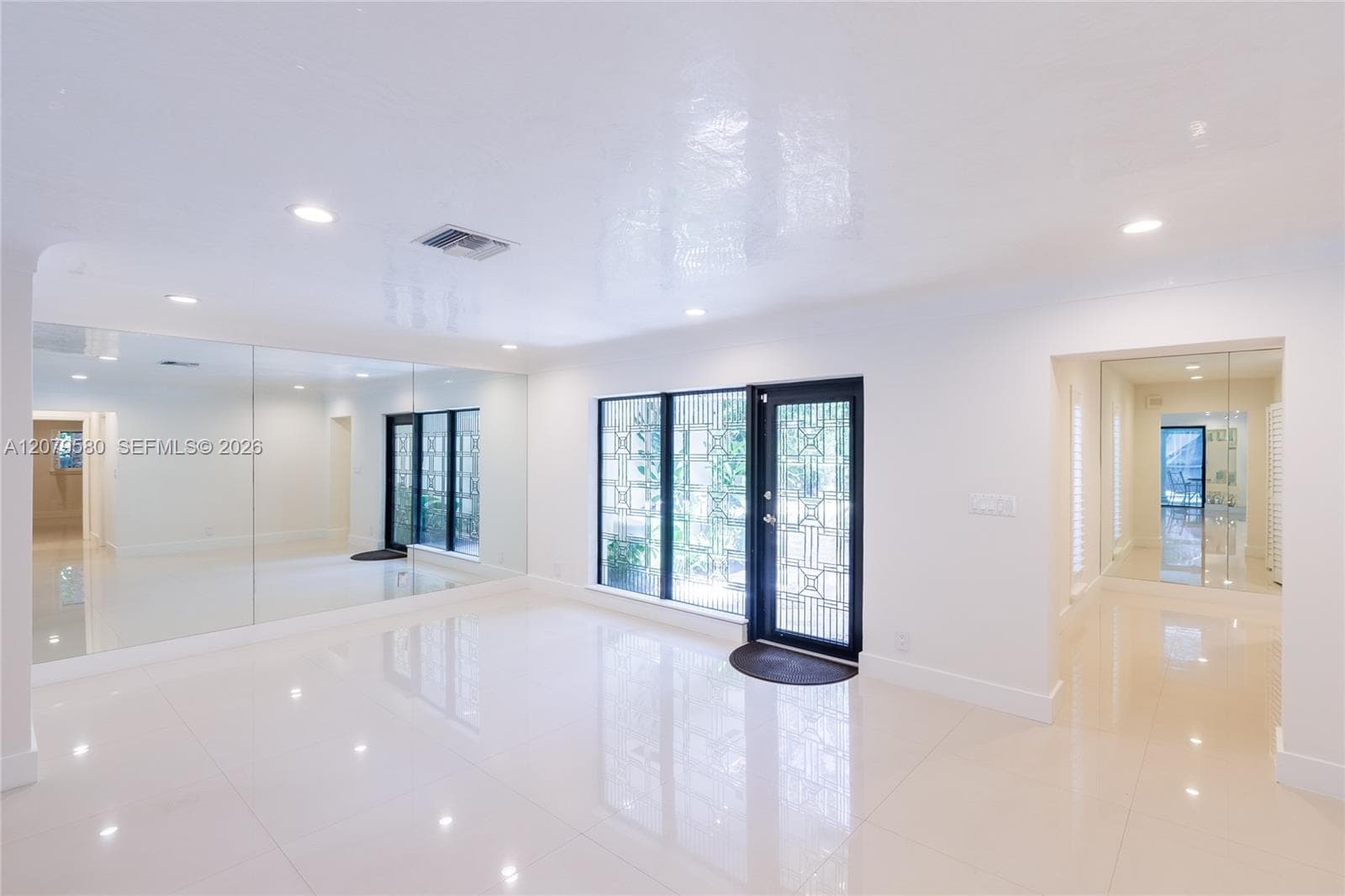 Polished tile flooring, wall-to-wall mirrors, recessed lighting, and a decorative metal-framed glass entry door