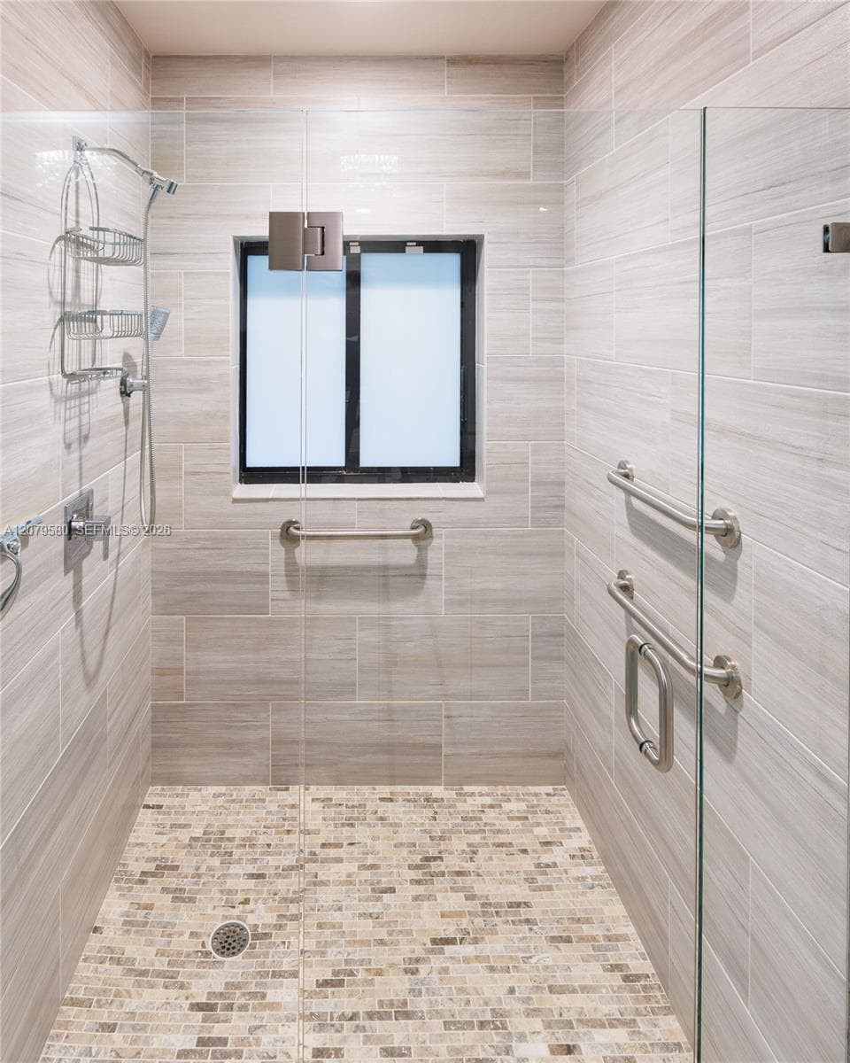 Walk-in shower featuring floor-to-ceiling tile, a glass door, mosaic tile flooring, and metal safety rails