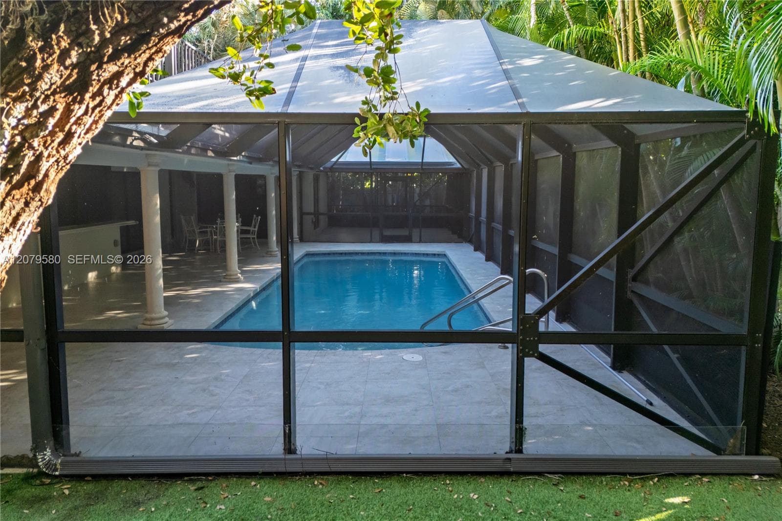 Screened enclosure featuring a rectangular swimming pool, a covered patio area with structural columns, and paved pool decking