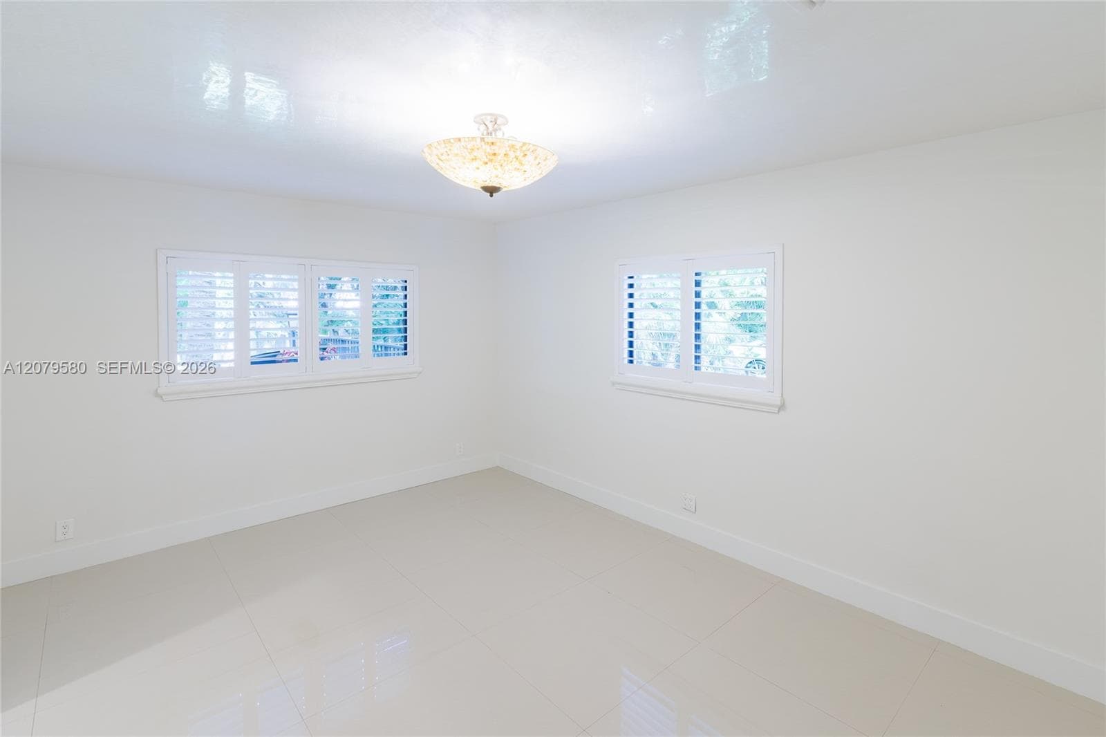 Interior space featuring neutral large-format tile flooring, dual windows with plantation shutters, and a decorative semi-flush mount ceiling light fixture